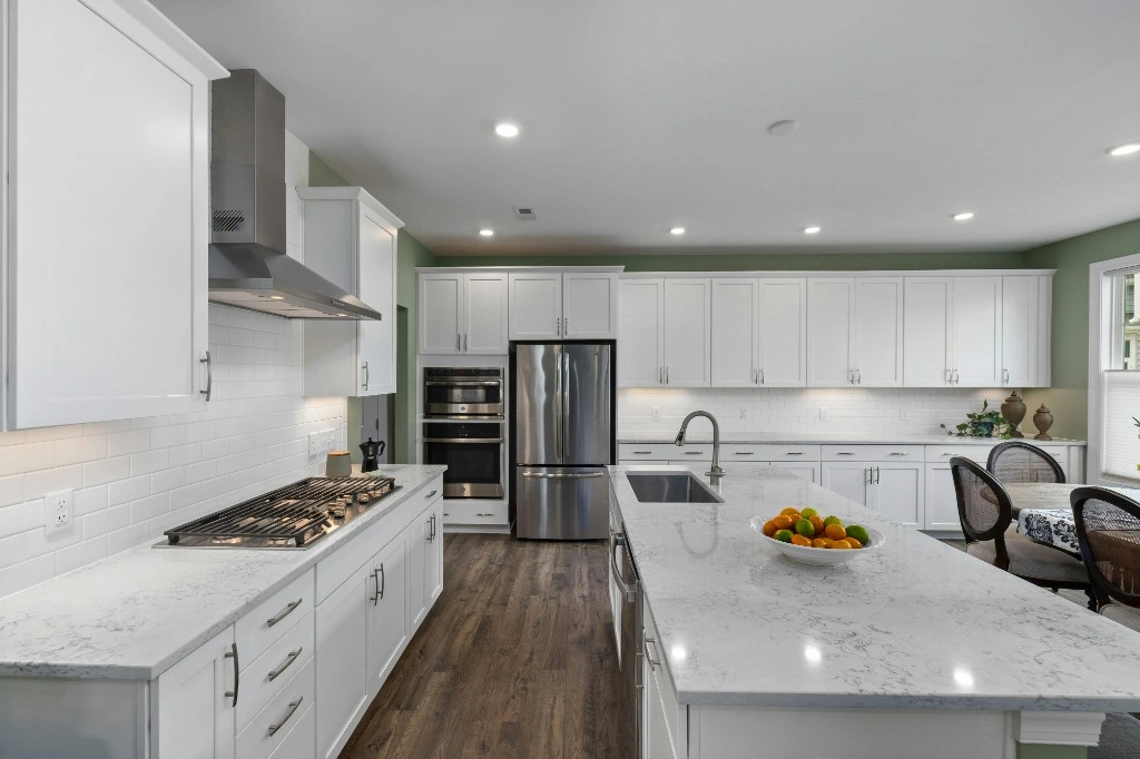 Immaculate open kitchen with white cabinets, quartz counters, and stainless appliances
